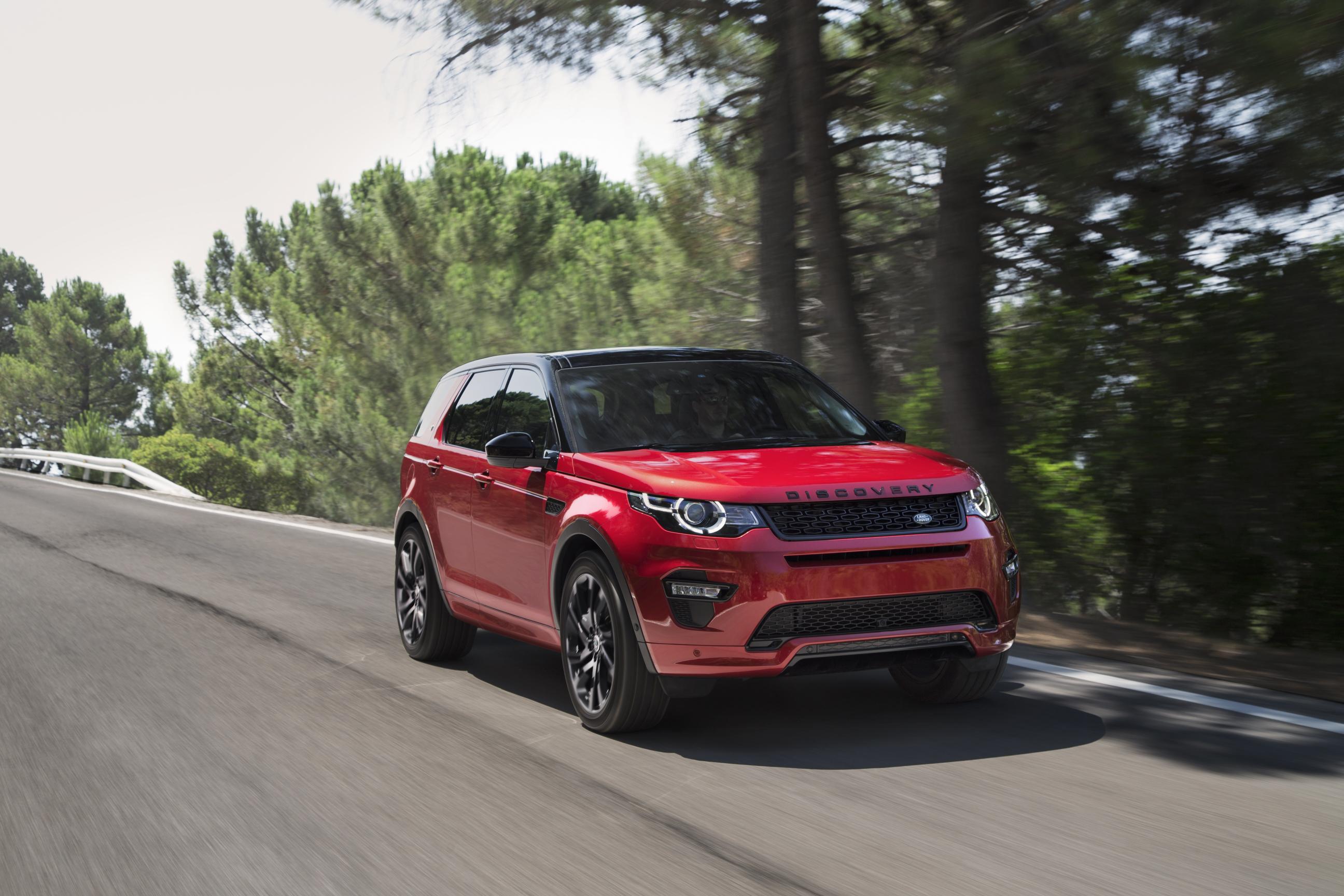 Red Land Rover Discovery Sport driving towards the right along a tree-lined road.